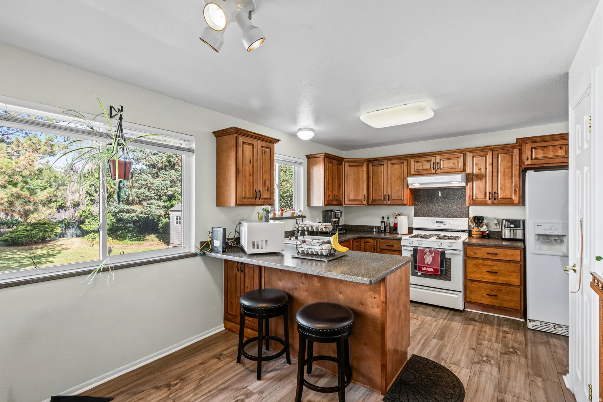 Kitchen featuring wood-finish flooring, natural wood cabinetry, a central island with a granite-style countertop, a white gas range, and a white refrigerator