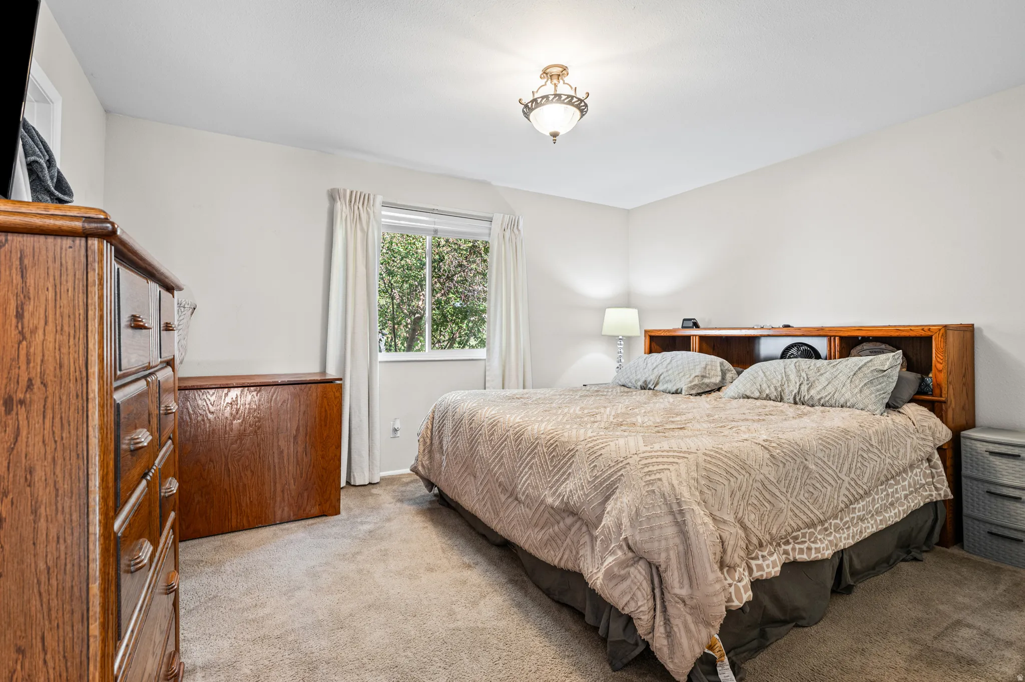 Carpeted bedroom with a single window and an overhead semi-flush mount light fixture
