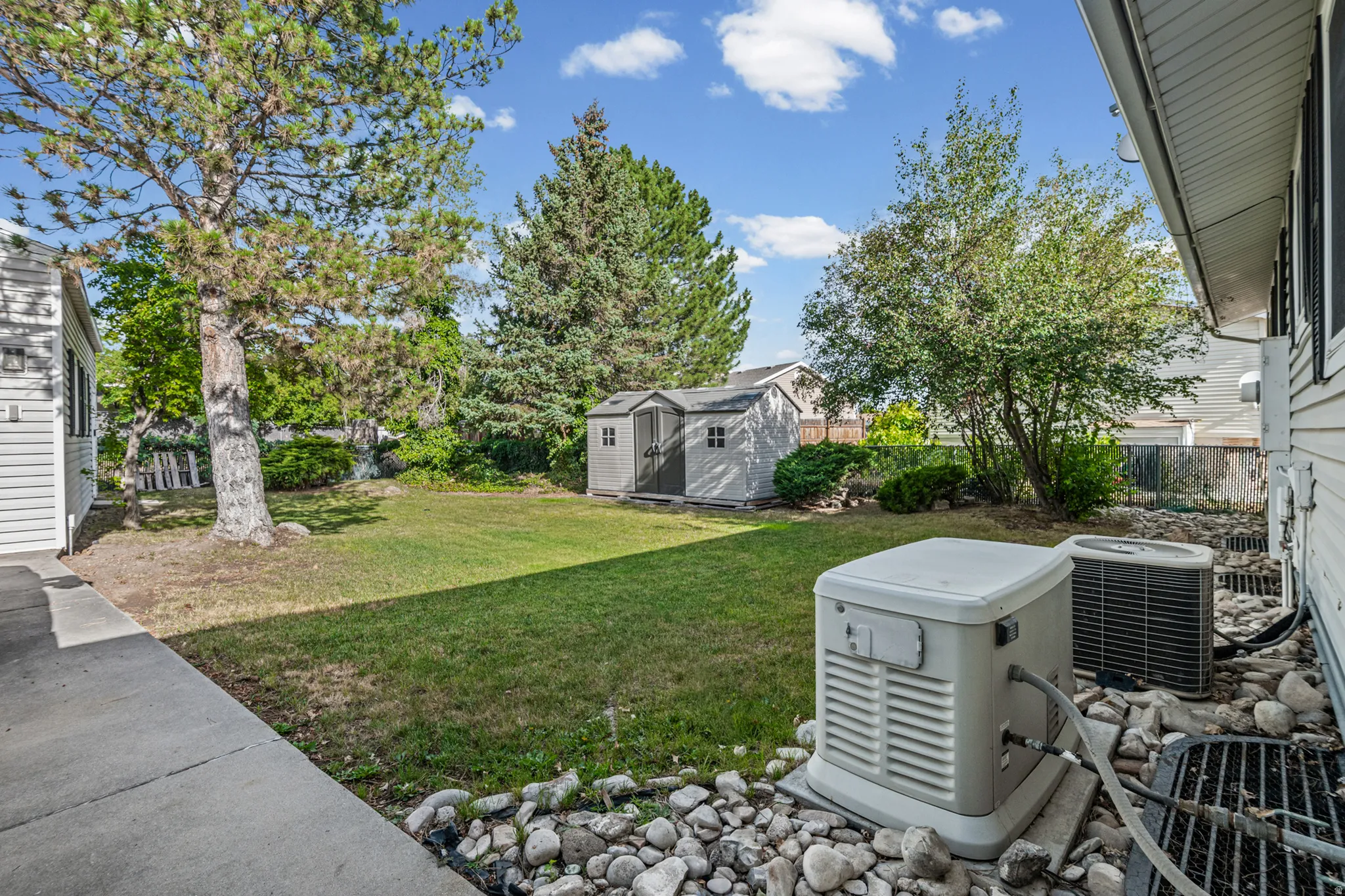 Expansive backyard featuring a lush lawn, mature trees, and a utility shed
