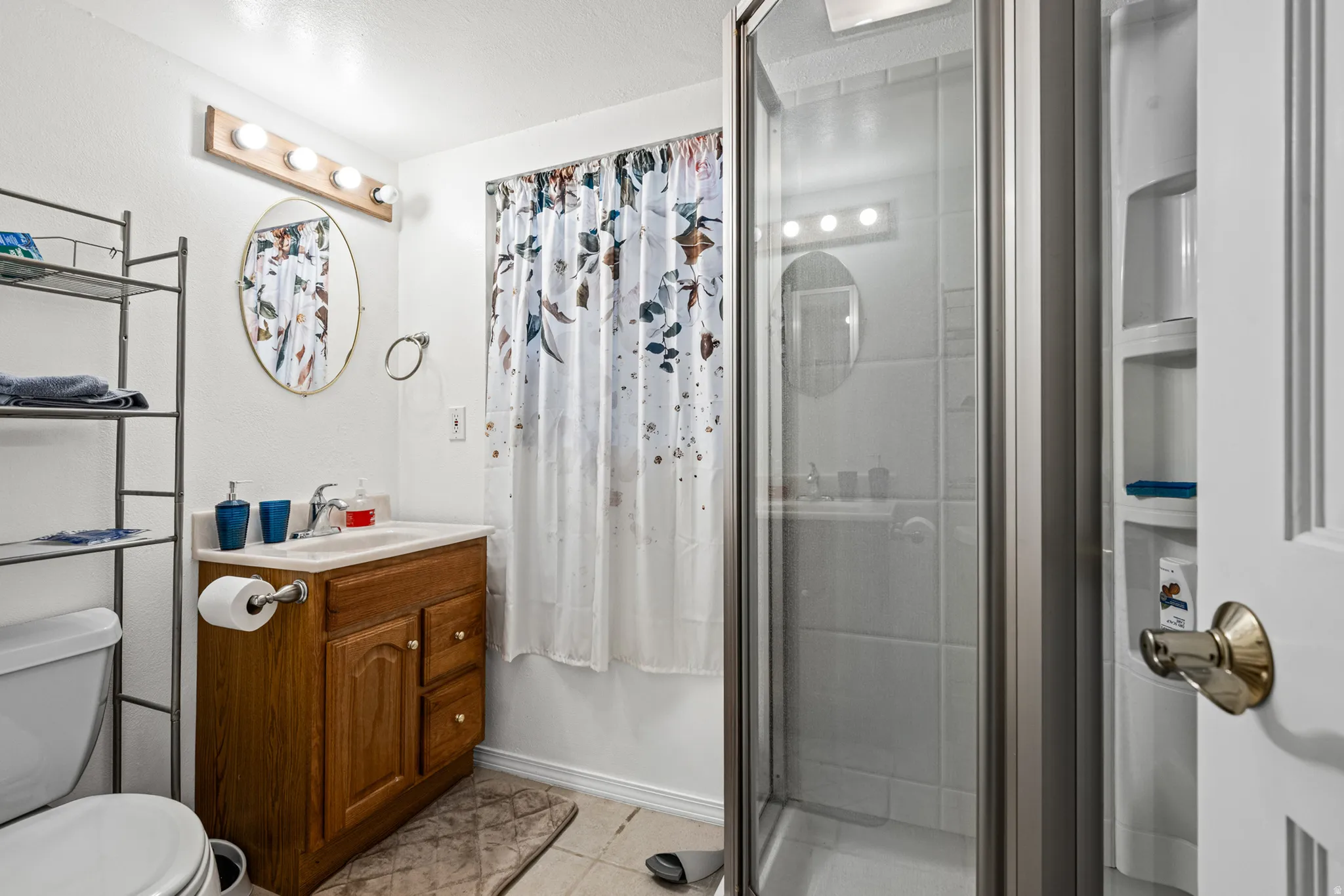 Bathroom featuring a glass-enclosed shower, wood-finish vanity with countertop sink, and an oval wall mirror