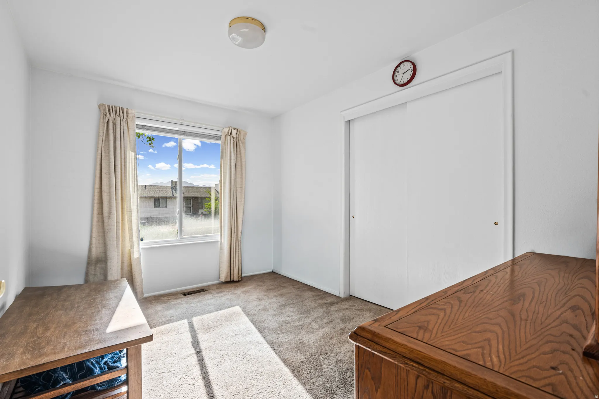 Carpeted interior space featuring a large window with drapes, a flush mount ceiling light, and a white sliding closet door