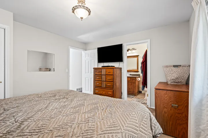Bedroom with white walls and a ceiling-mounted light fixture, featuring a recessed wall niche, a paneled door, and wood-finish flooring