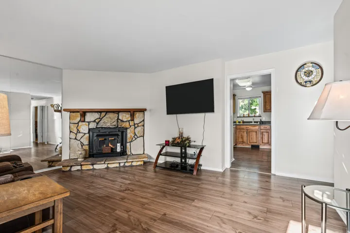 Living space featuring wood-finish flooring, a stone fireplace with a wood mantel, and white walls