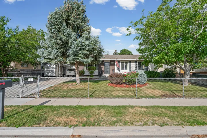 Ranch-style residence featuring a gray exterior with white trim, a gabled roof, and a chain-link fence enclosing the front yard