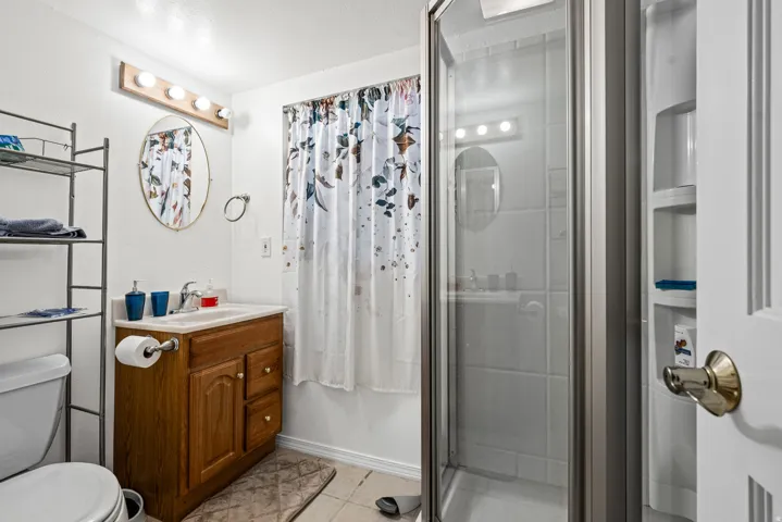Bathroom featuring a glass-enclosed shower, wood-finish vanity with countertop sink, and an oval wall mirror