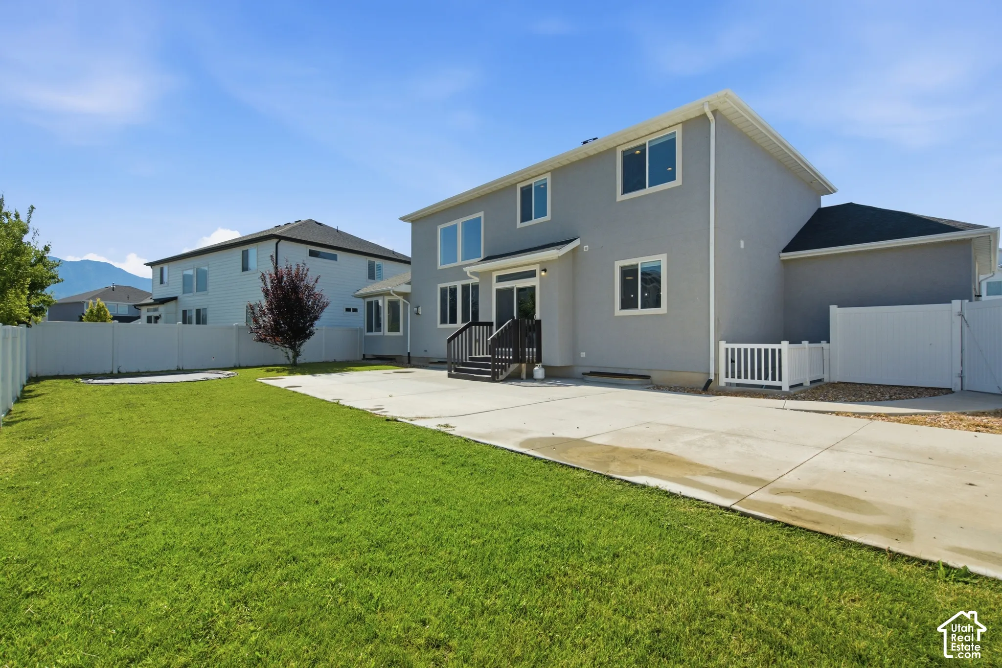 Expansive backyard featuring a manicured lawn, concrete patio, and white vinyl perimeter fencing