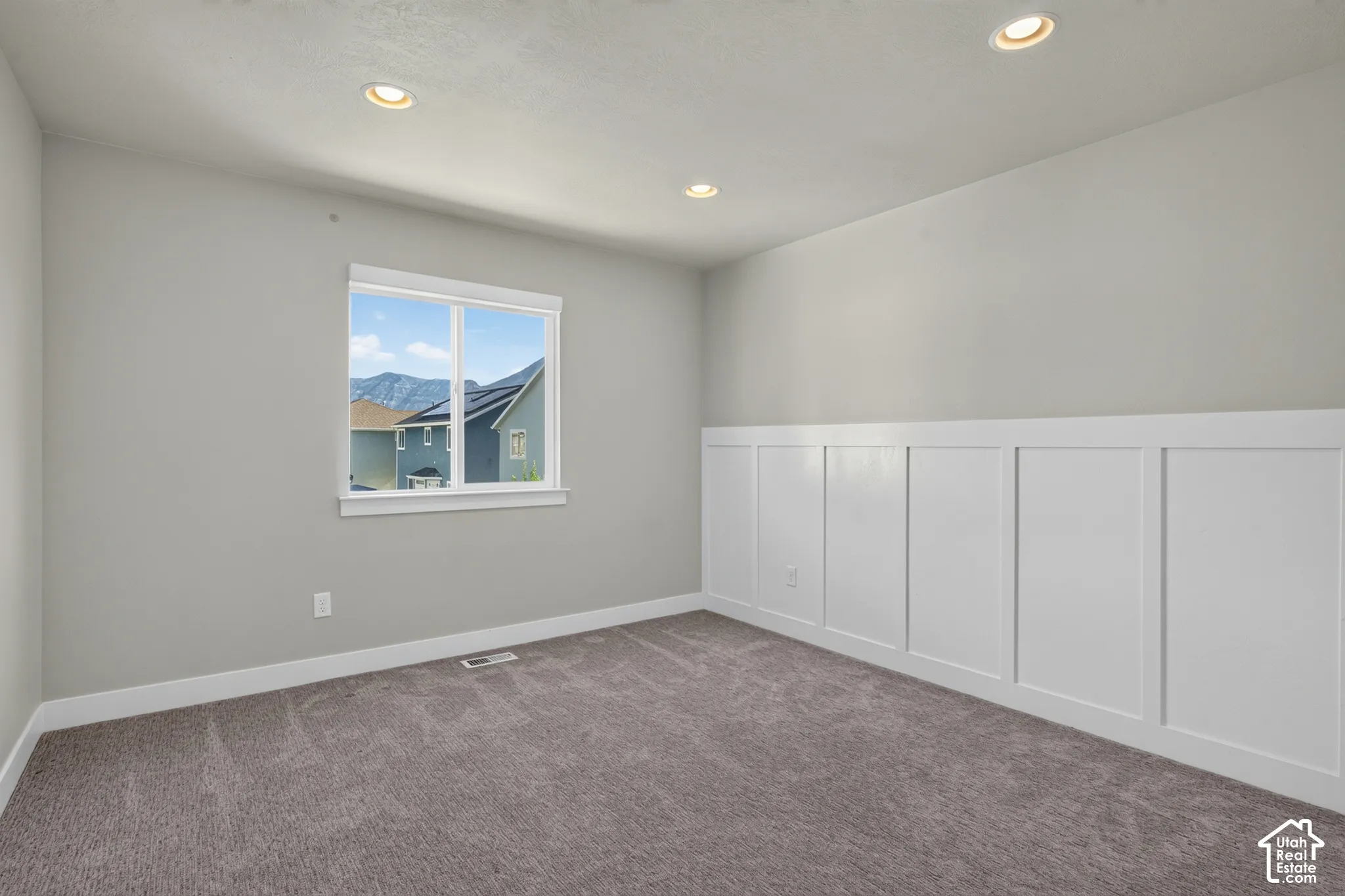 Neutral painted walls with recessed lighting, a single window, and a white wainscoting accent wall