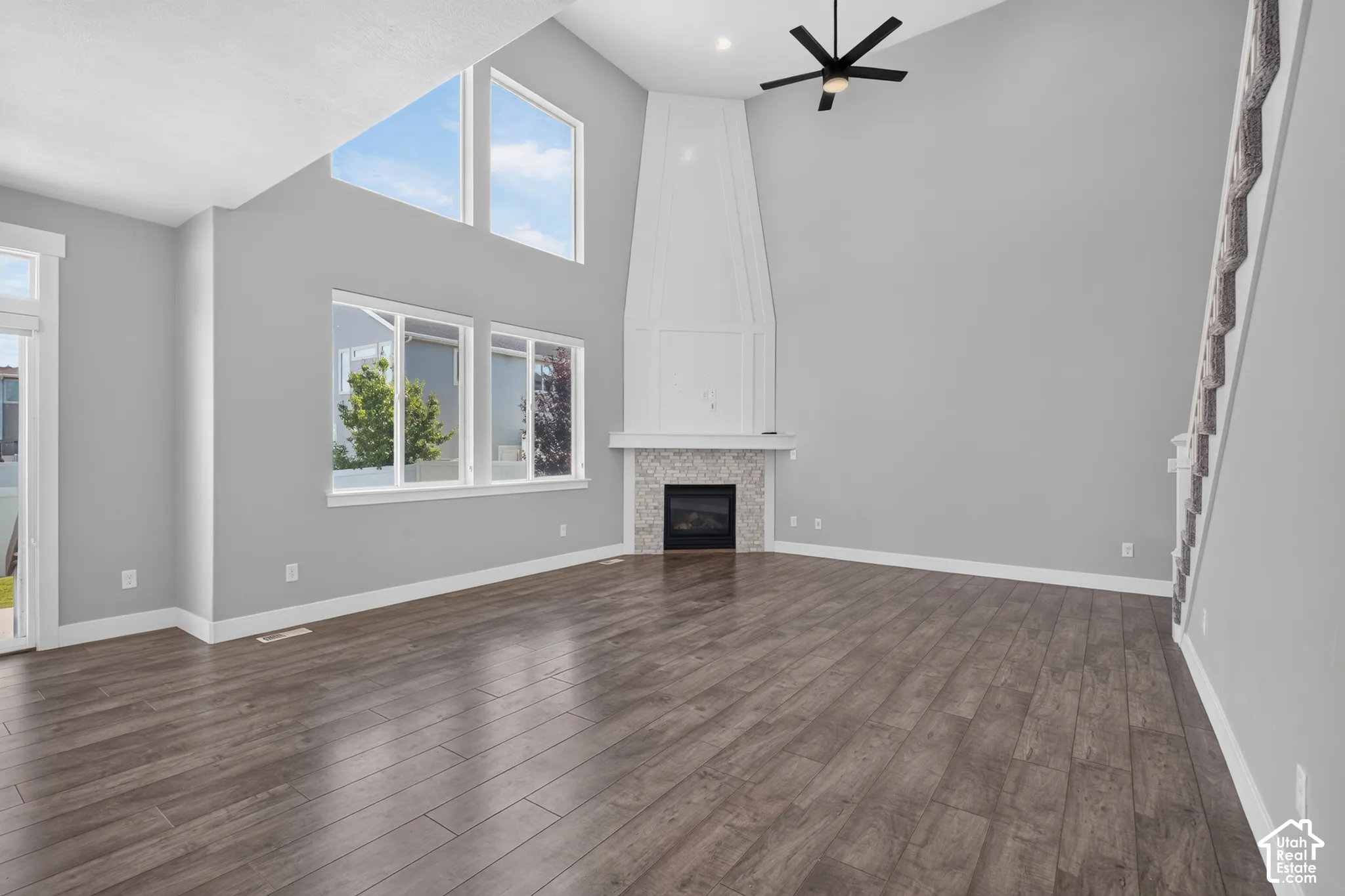 Spacious living area featuring high vaulted ceilings, expansive windows, wood-finish flooring, a contemporary ceiling fan, and a built-in fireplace with a tiled surround