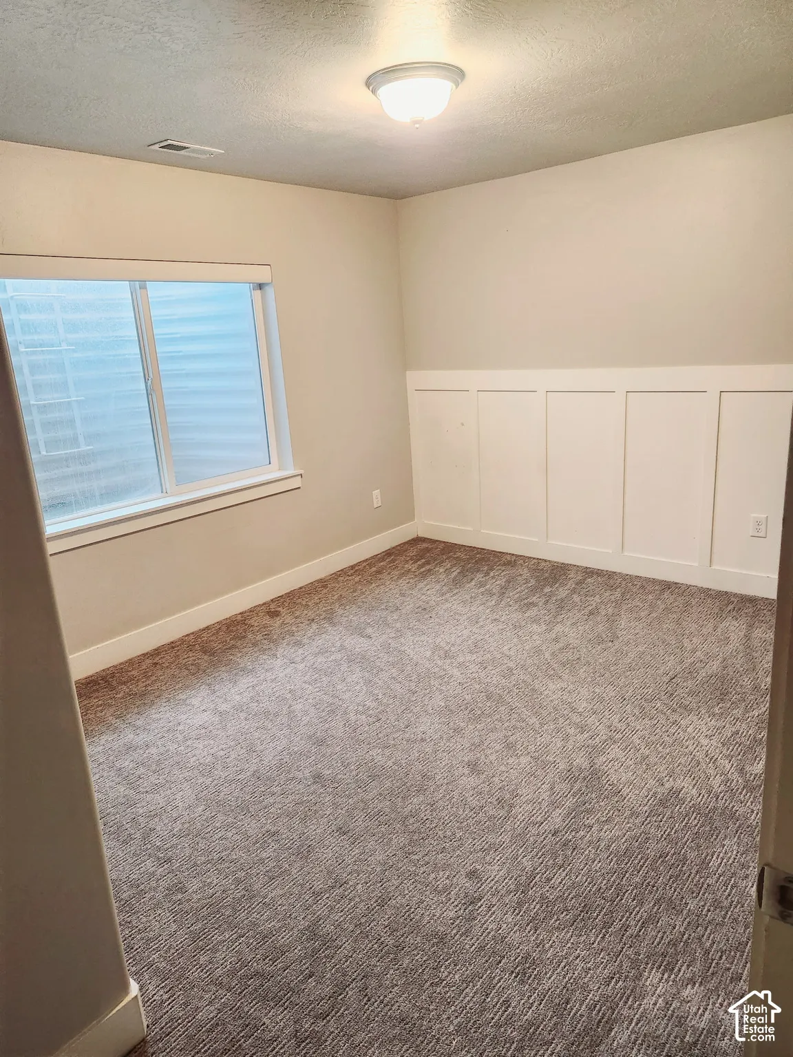 Carpeted room featuring a window with blinds, baseboard trim, and wainscoting