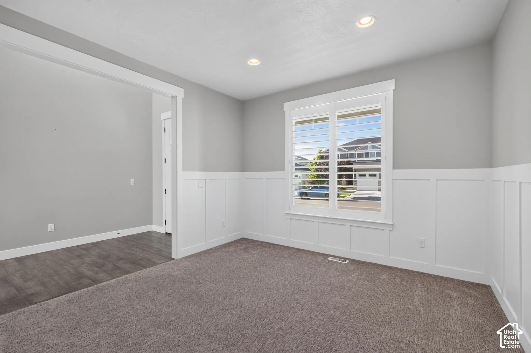 Bright interior space featuring a window with plantation shutters, recessed lighting, and wainscoting