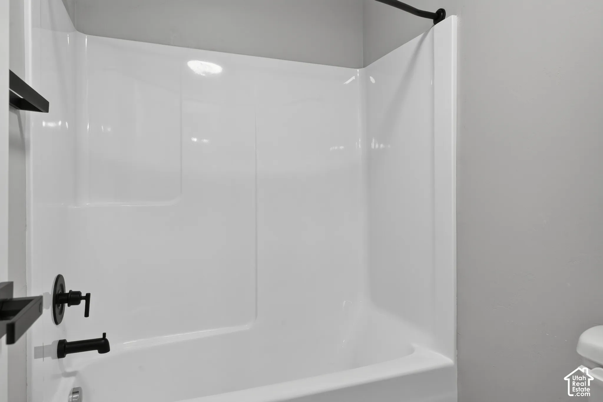 Bathtub and shower combination featuring a white surround, matte black fixtures, and a matte black shower curtain rod