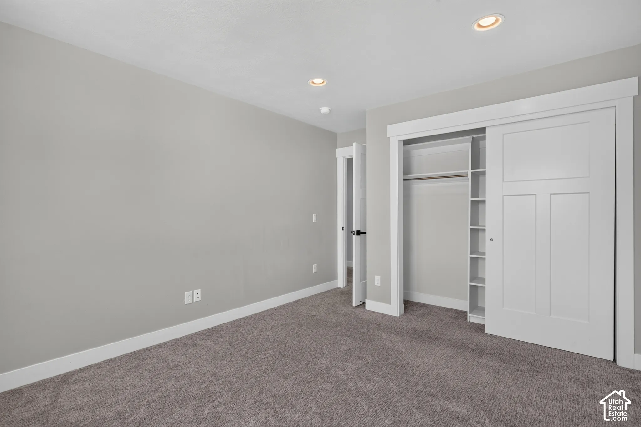 Recessed lighting illuminates a neutral gray room featuring soft gray carpeting, white baseboards, and a white interior door