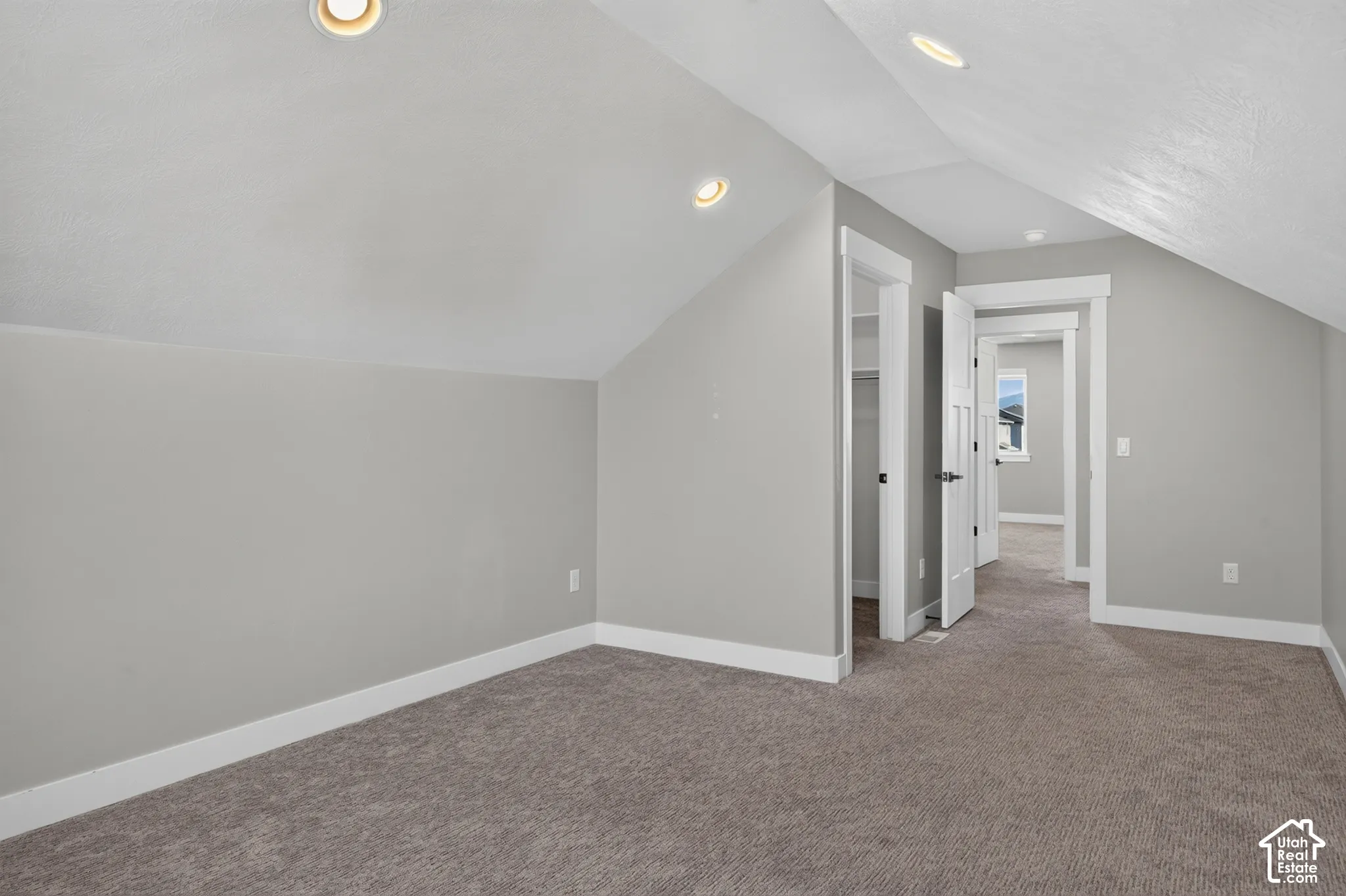 Carpeted room featuring sloped ceilings, recessed lighting, and white baseboards