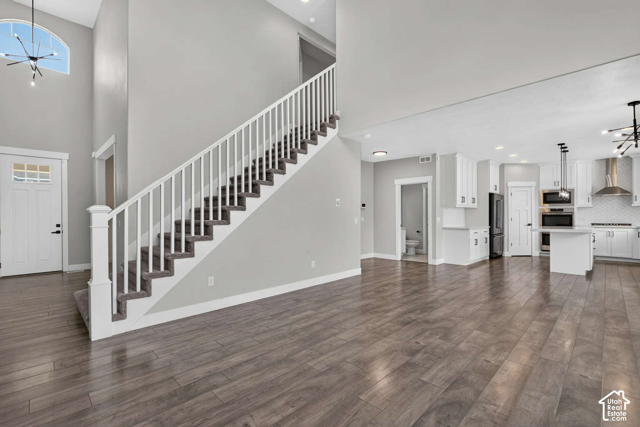 Open-concept living area featuring wood-finish flooring, a contemporary white kitchen with black appliances, a central island, and a built-in oven and microwave