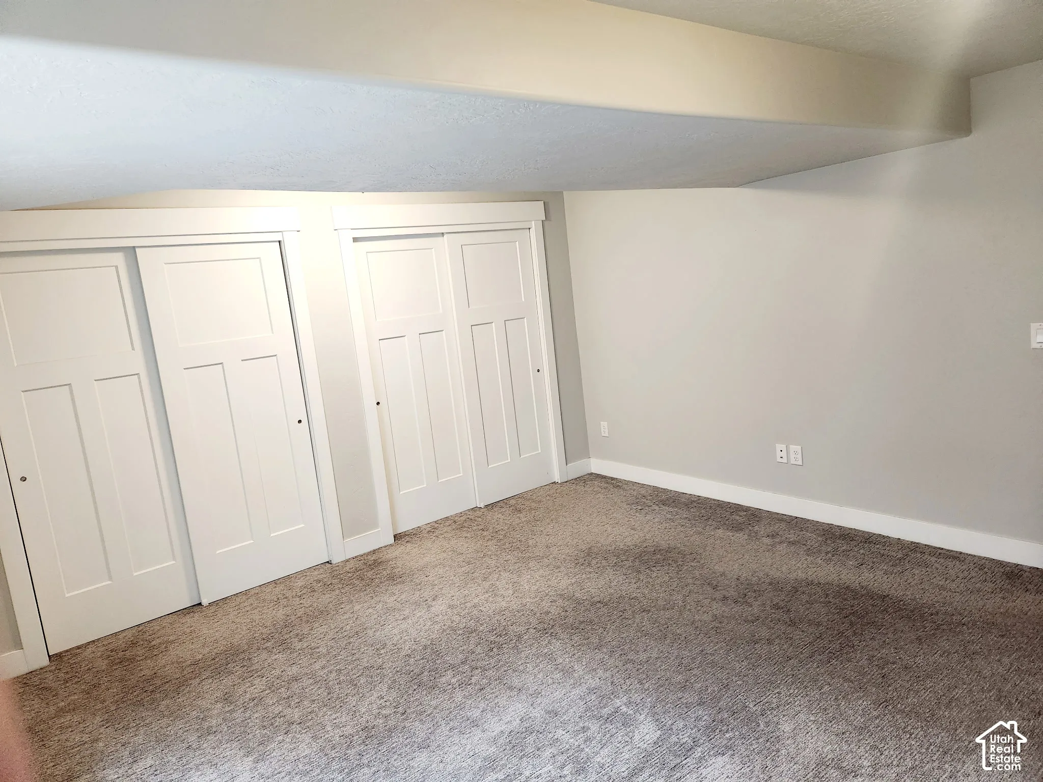 Room featuring white sliding closet doors, light gray wall paint, white baseboards, and neutral-toned carpet flooring