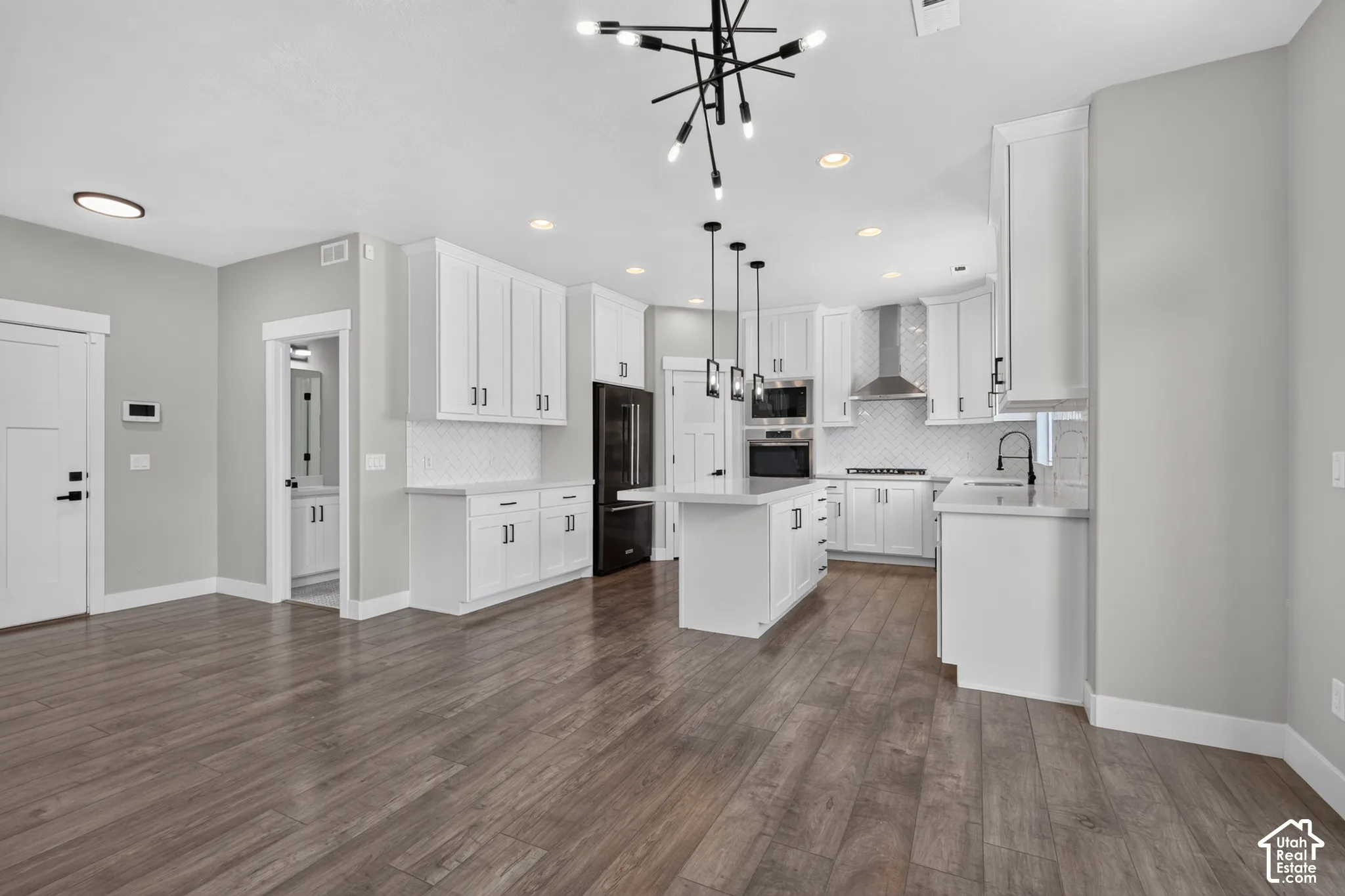 Contemporary open-concept kitchen featuring white cabinetry, an island with pendant lighting, stainless steel appliances, and wood-finish flooring