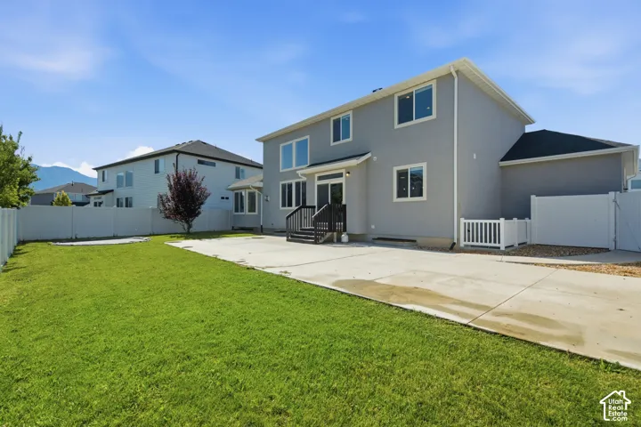 Expansive backyard featuring a manicured lawn, concrete patio, and white vinyl perimeter fencing