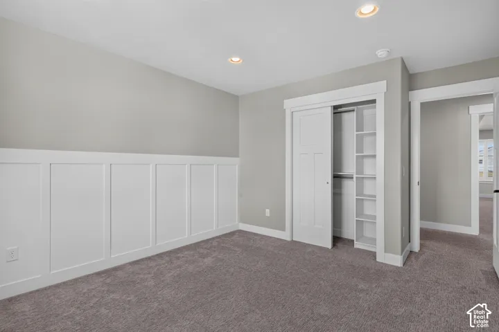 Carpeted room featuring wainscoting, recessed lighting, and a closet with bifold doors and built-in shelving