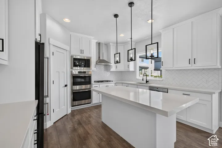 Contemporary kitchen featuring an oversized island with a solid surface countertop, white shaker cabinetry, stainless steel appliances, herringbone tile backsplash, and wood-finish flooring