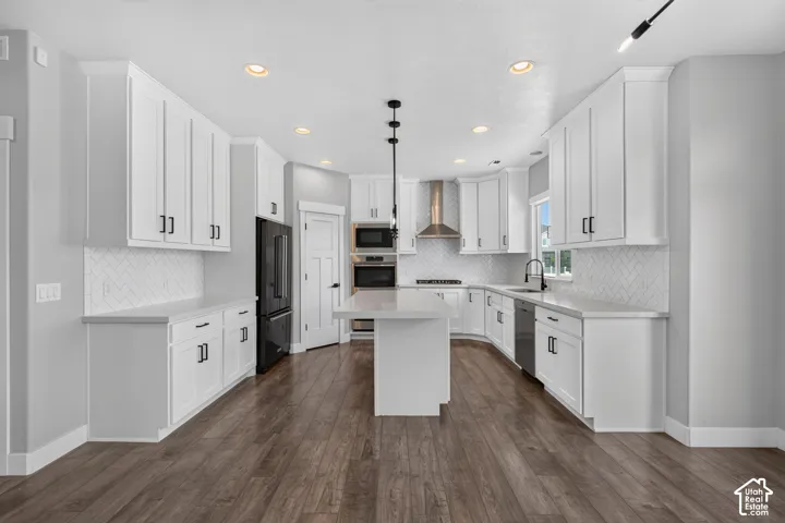 Spacious kitchen featuring white cabinetry, a large central island, stainless steel appliances, herringbone tile backsplash, and wood-finish flooring