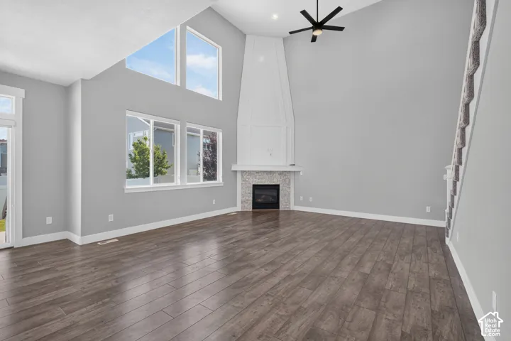 Spacious living area featuring high vaulted ceilings, expansive windows, wood-finish flooring, a contemporary ceiling fan, and a built-in fireplace with a tiled surround