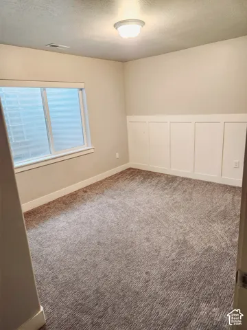 Carpeted room featuring a window with blinds, baseboard trim, and wainscoting
