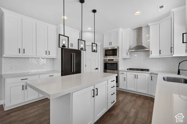 White shaker cabinetry with dark hardware, quartz countertops, a herringbone tile backsplash, wood-finish flooring, and stainless steel appliances