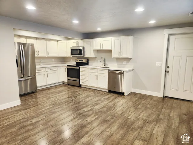 Kitchen with wood-finish flooring, white cabinetry, light countertops, and recessed lighting