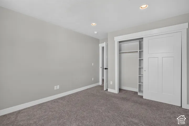 Recessed lighting illuminates a neutral gray room featuring soft gray carpeting, white baseboards, and a white interior door