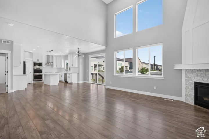 Open-concept living area with wood-finish flooring, a two-story vaulted ceiling, and a fireplace featuring a stone surround and a white mantle