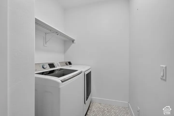 Dedicated laundry area featuring a white wall shelf with a hanging rod, white walls, and hexagonal floor tiling