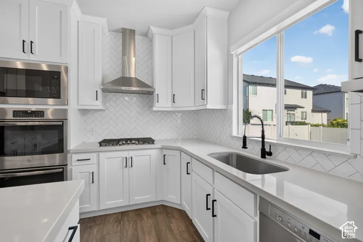 Modern kitchen featuring white shaker cabinetry, stainless steel appliances, a herringbone tile backsplash, an undermount sink with a gooseneck faucet, and wood-finish flooring