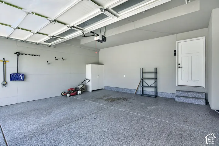 Spacious garage featuring a durable epoxy-coated floor, automatic garage door opener, and a side entry door with integrated steps