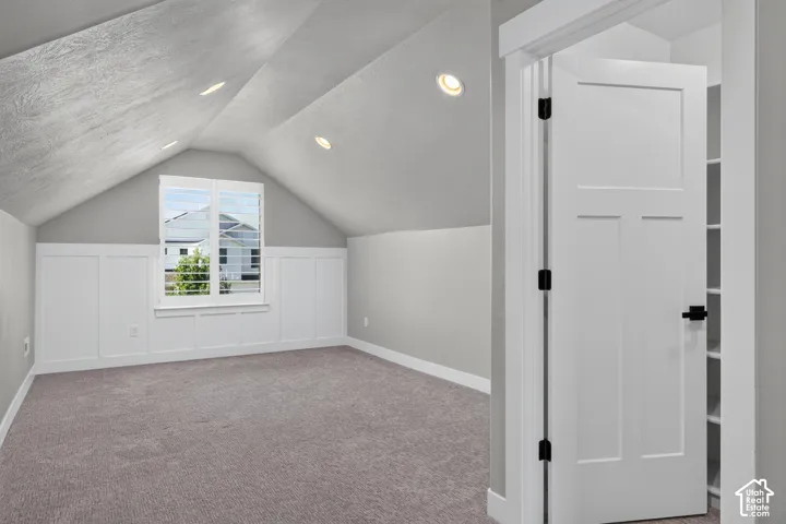 Room featuring an angled ceiling with recessed lighting, board and batten wall detailing, a window with louvered blinds, and gray carpeting