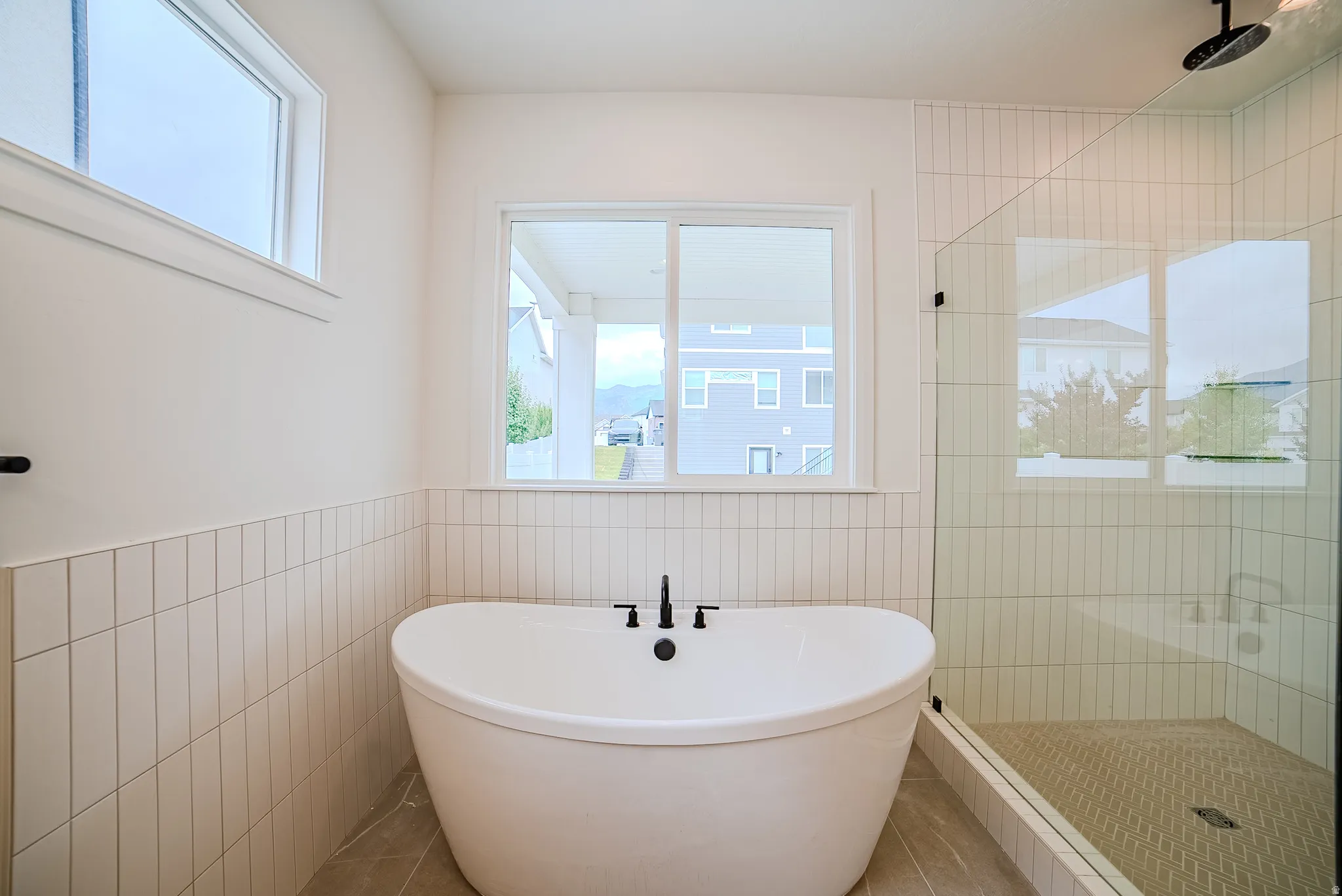 Freestanding soaking tub with matte black fixtures, framed by vertical stacked tile wainscoting