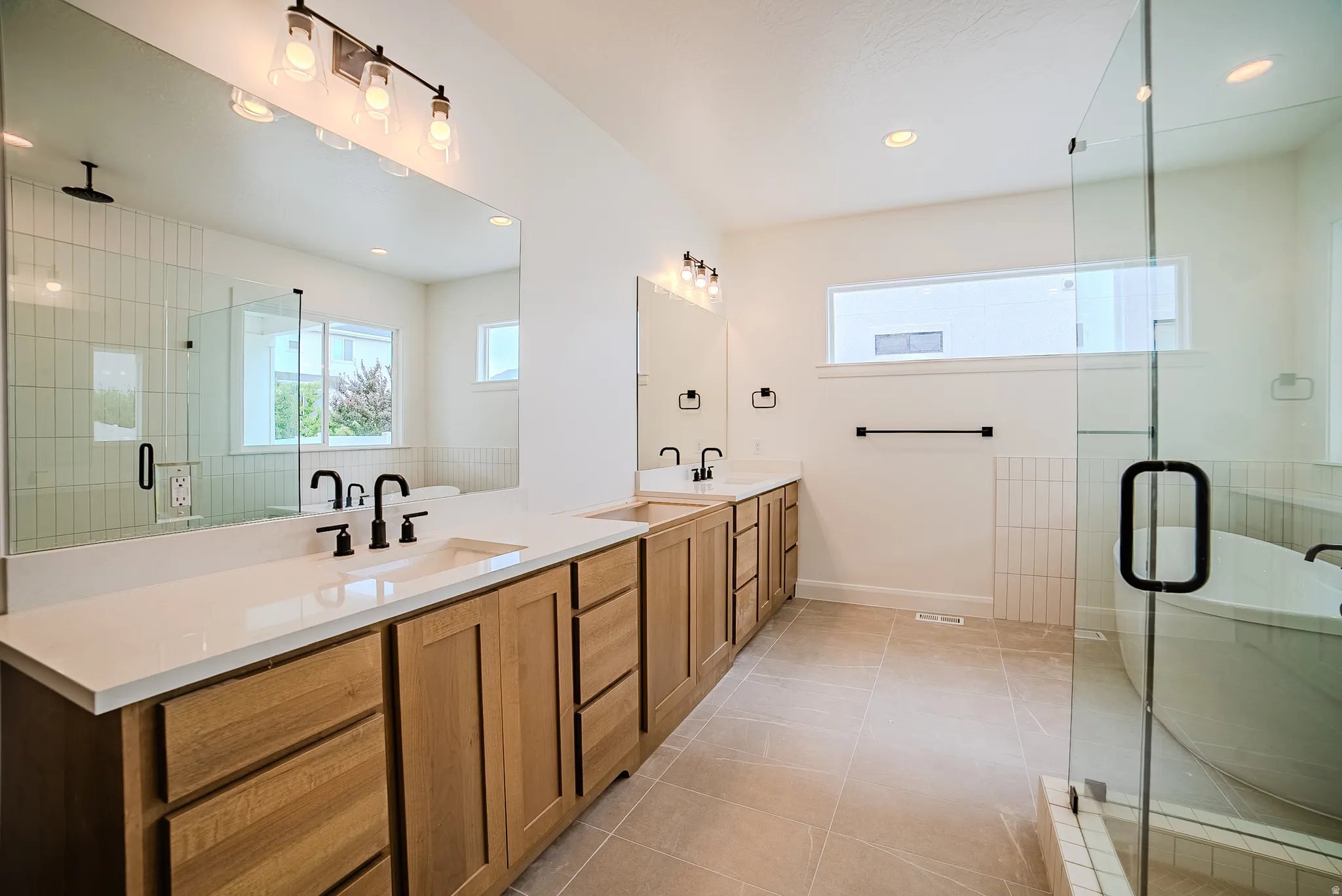 Dual vanity with wood-finish cabinetry, white countertops, and matte black fixtures