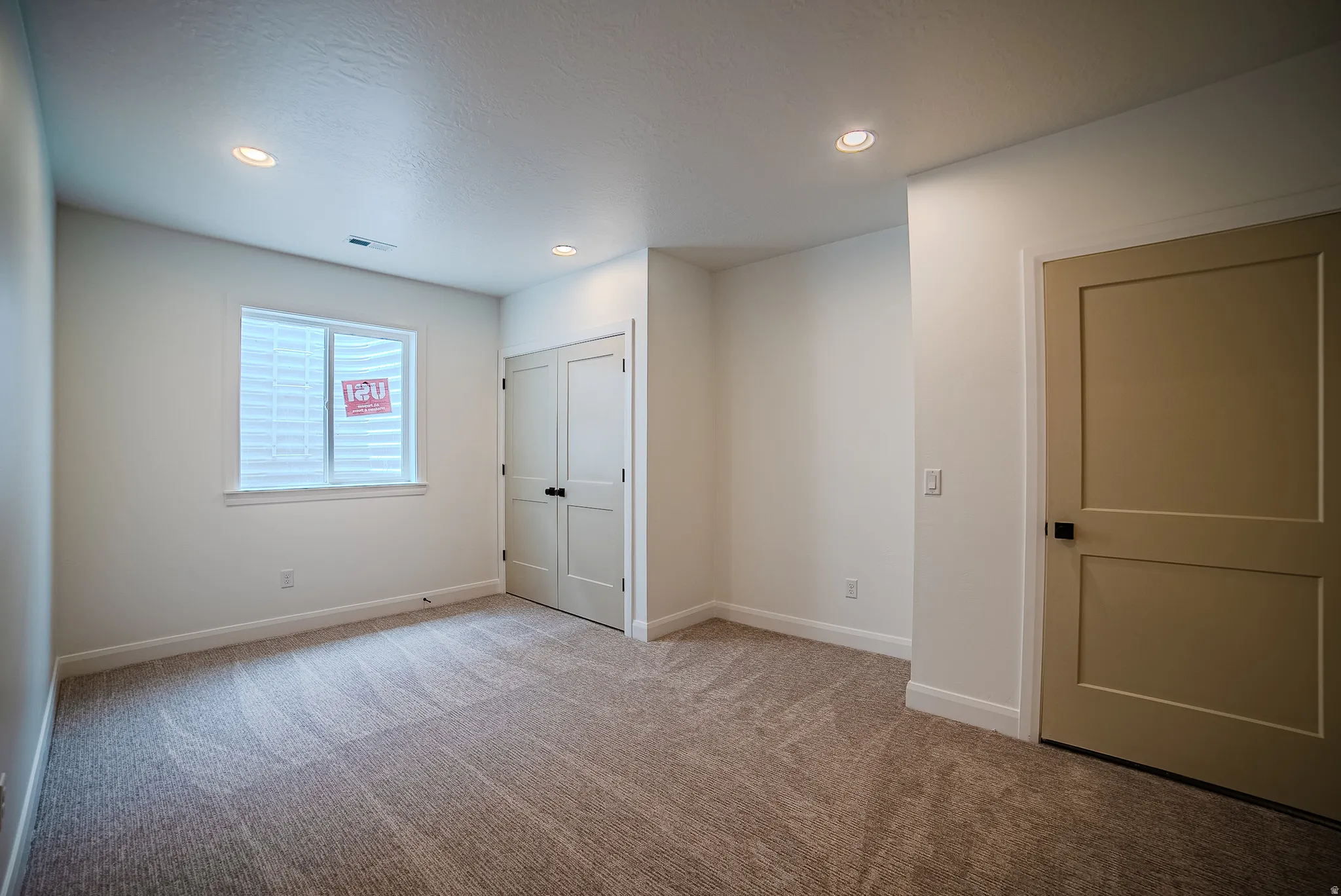Carpeted room featuring recessed lighting, a neutral wall color, a white-framed window with white blinds, a bi-fold closet door, and a solid panel door with black hardware