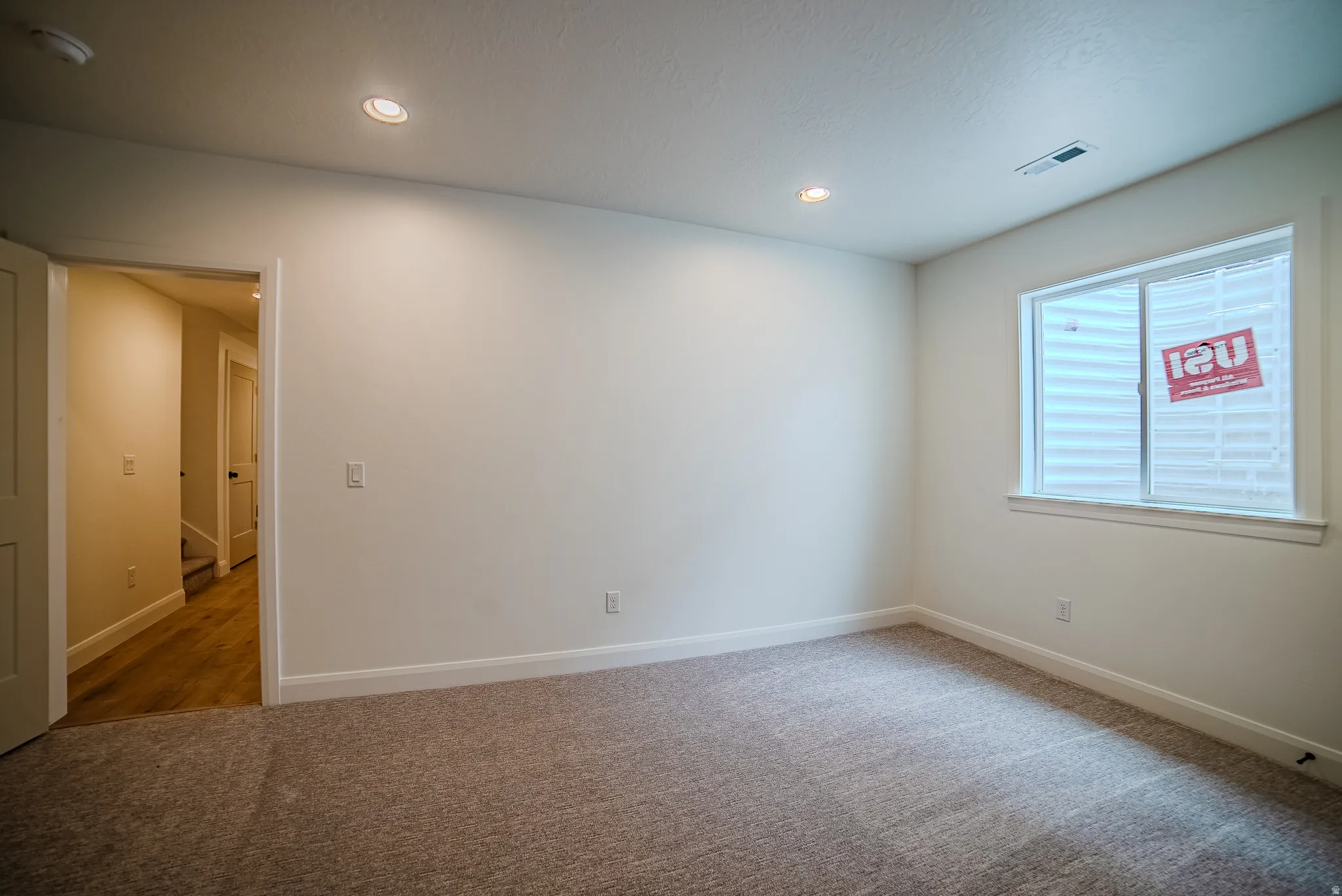 Spacious room featuring neutral carpeting, recessed lighting, white walls, and a window with white trim