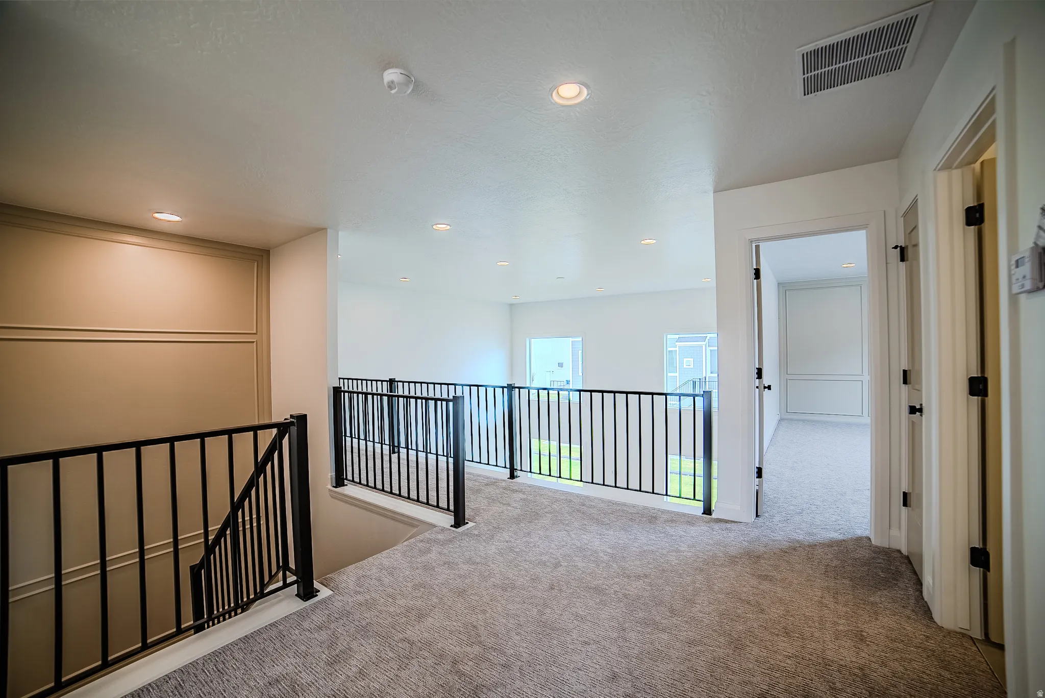 Upper-level landing featuring a carpeted floor, recessed lighting, and black metal railings
