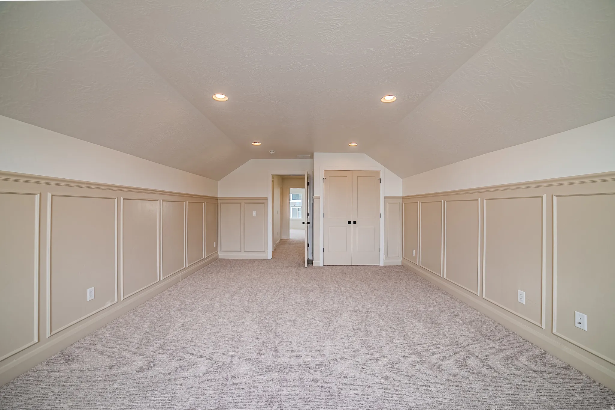 Spacious room featuring vaulted ceilings, recessed lighting, wall paneling, light-toned carpeting, and double-door closet