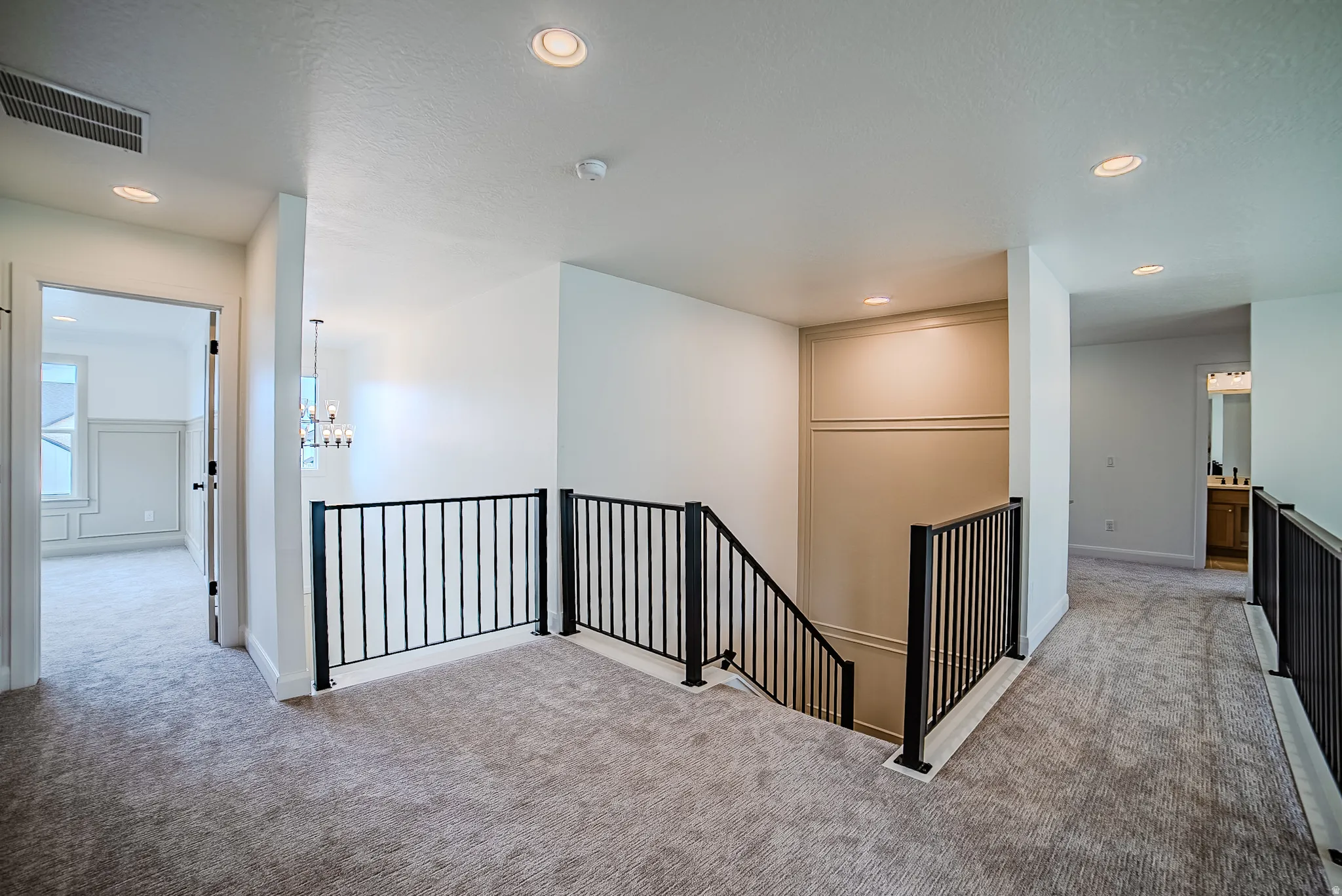 Carpeted upper-level landing featuring black metal railings and recessed lighting