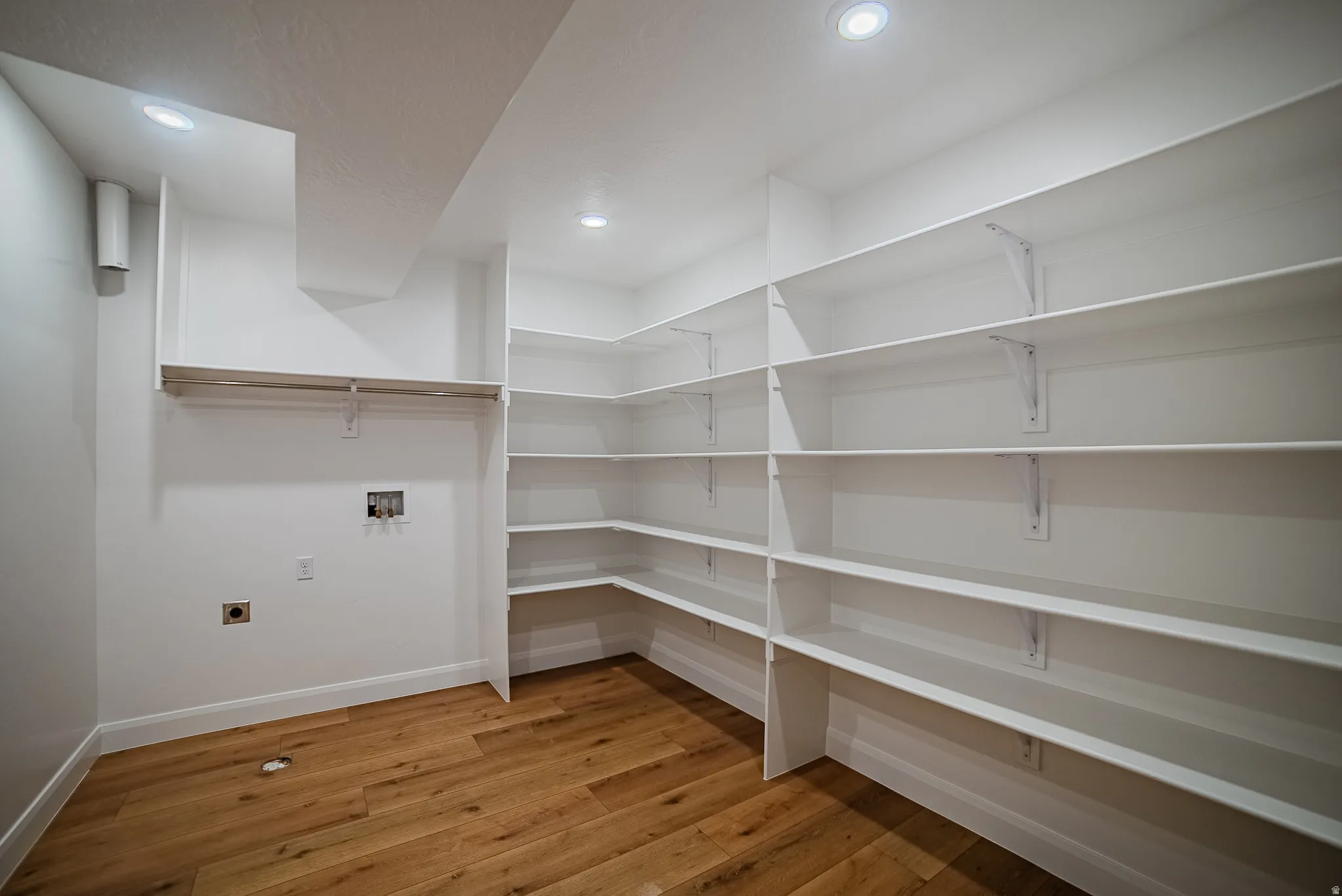 Utility room featuring extensive built-in shelving, wood-finish flooring, recessed lighting, and a clothes hanging rod