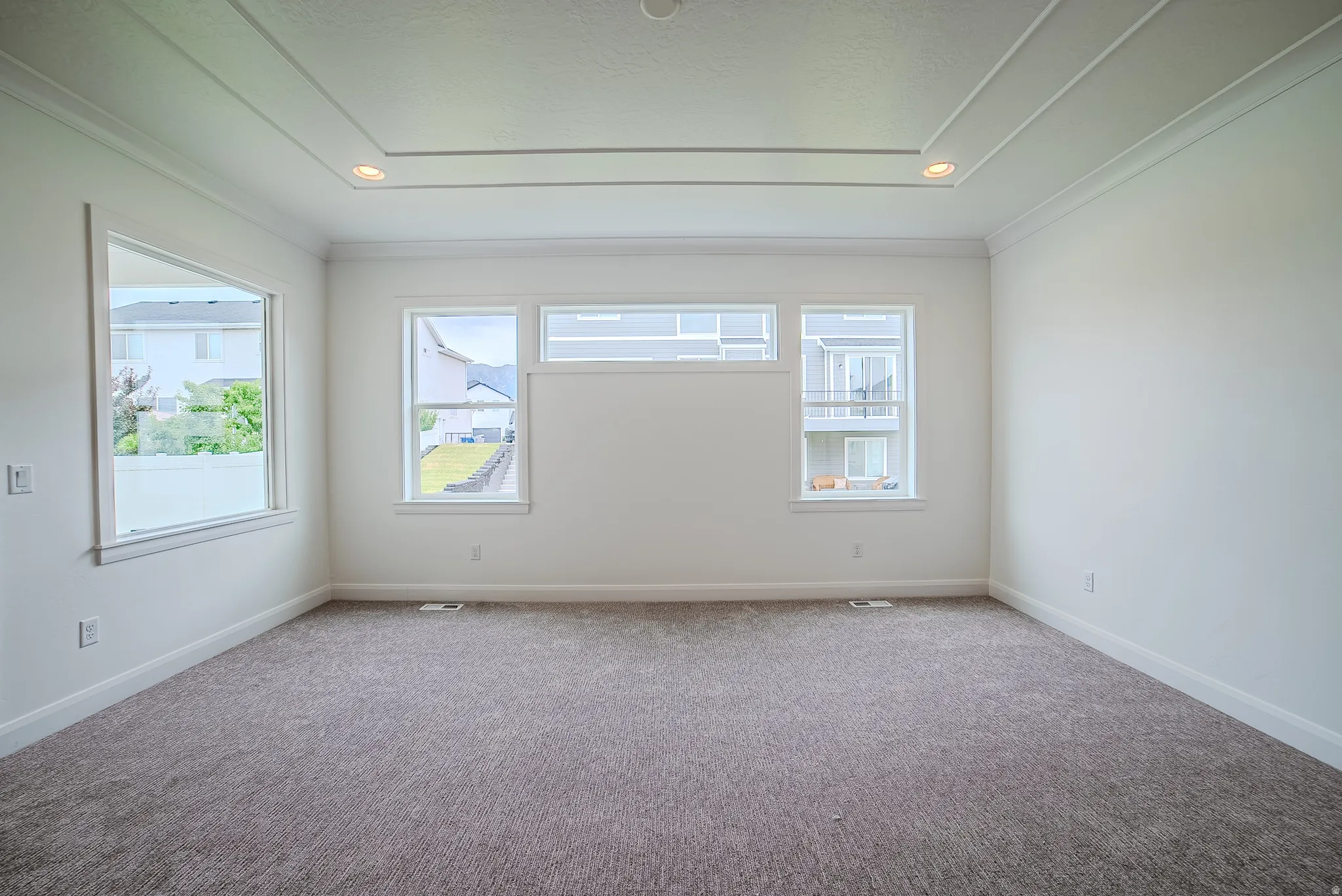 Spacious room with tray ceiling, recessed lighting, white walls, multiple windows, and neutral carpet