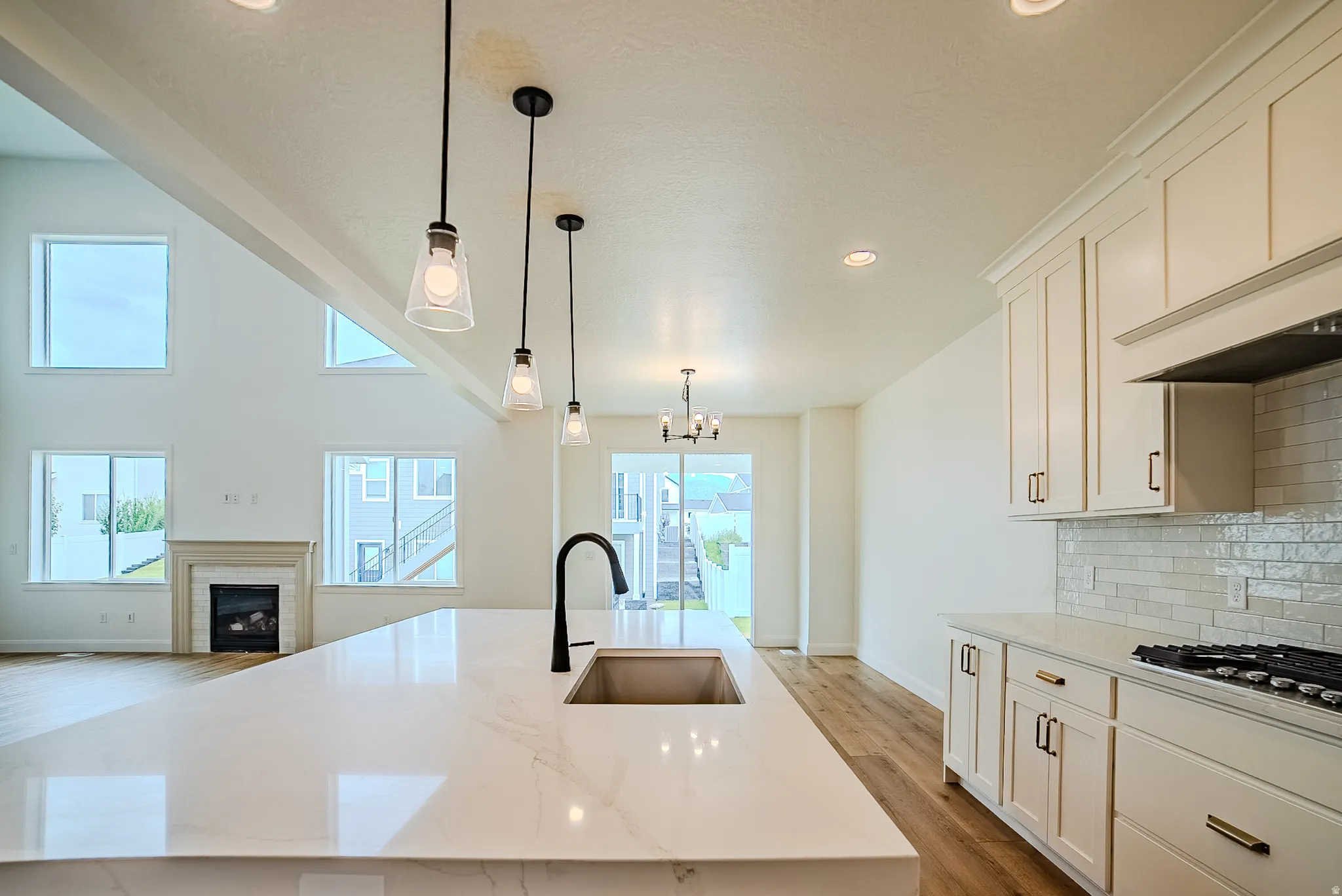 Spacious kitchen island with an undermount sink and matte black faucet, featuring white cabinetry, a tiled backsplash, and recessed lighting