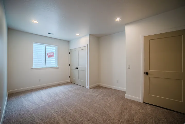 Carpeted room featuring recessed lighting, a neutral wall color, a white-framed window with white blinds, a bi-fold closet door, and a solid panel door with black hardware