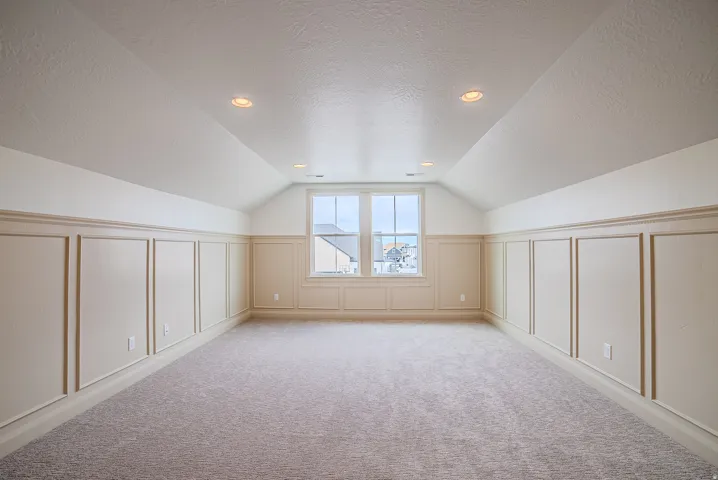 Spacious room featuring sloped ceilings, recessed lighting, and wainscoting paneling
