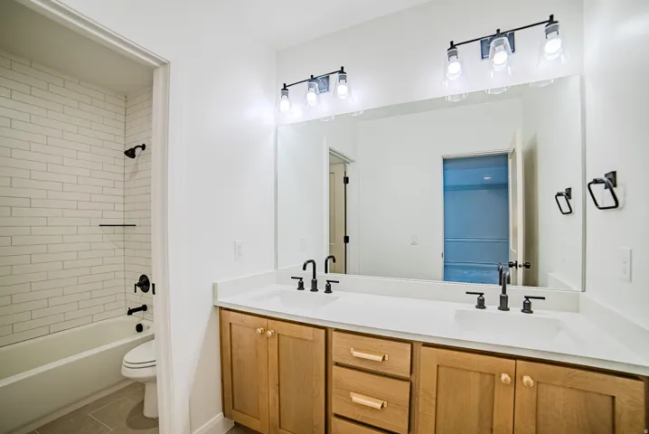 Dual vanity with light wood cabinetry, white countertops, and matte black fixtures