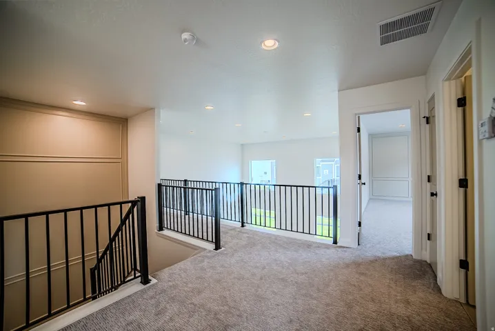 Upper-level landing featuring a carpeted floor, recessed lighting, and black metal railings