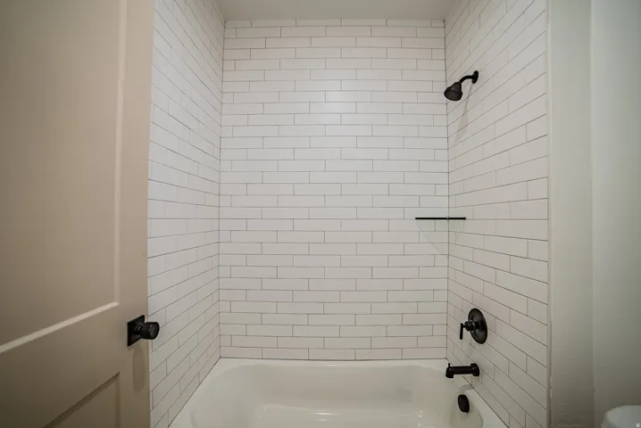 Bathtub shower combination featuring white subway tile surround, matte black shower fixtures, and an integrated black shelf
