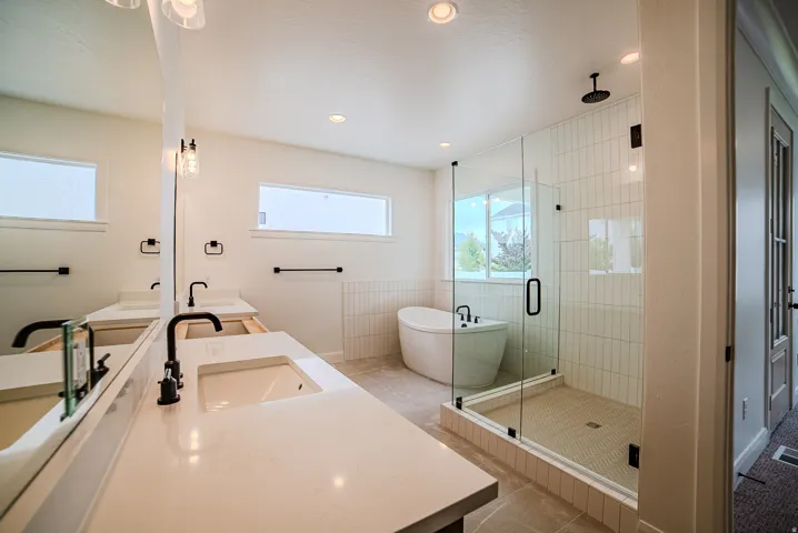 Modern bathroom featuring a dual vanity with undermount sinks and matte black fixtures, a freestanding soaking tub, and a glass-enclosed shower with subway tile surround and rain shower head
